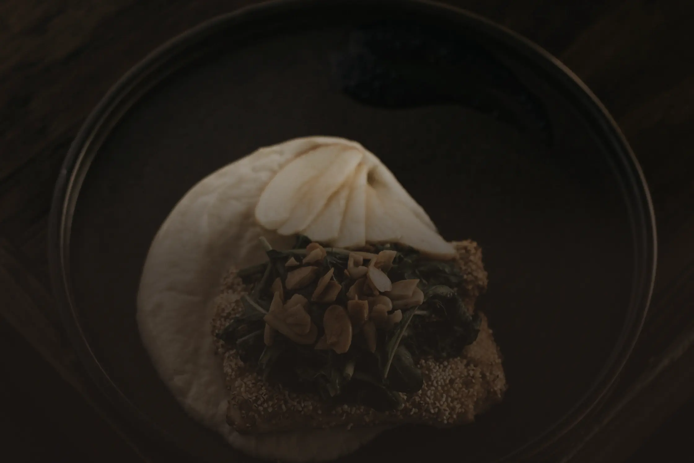 Une assiette de grès sombre vue du dessus : un pavé pané sur un lit de verdure et une crème claire.