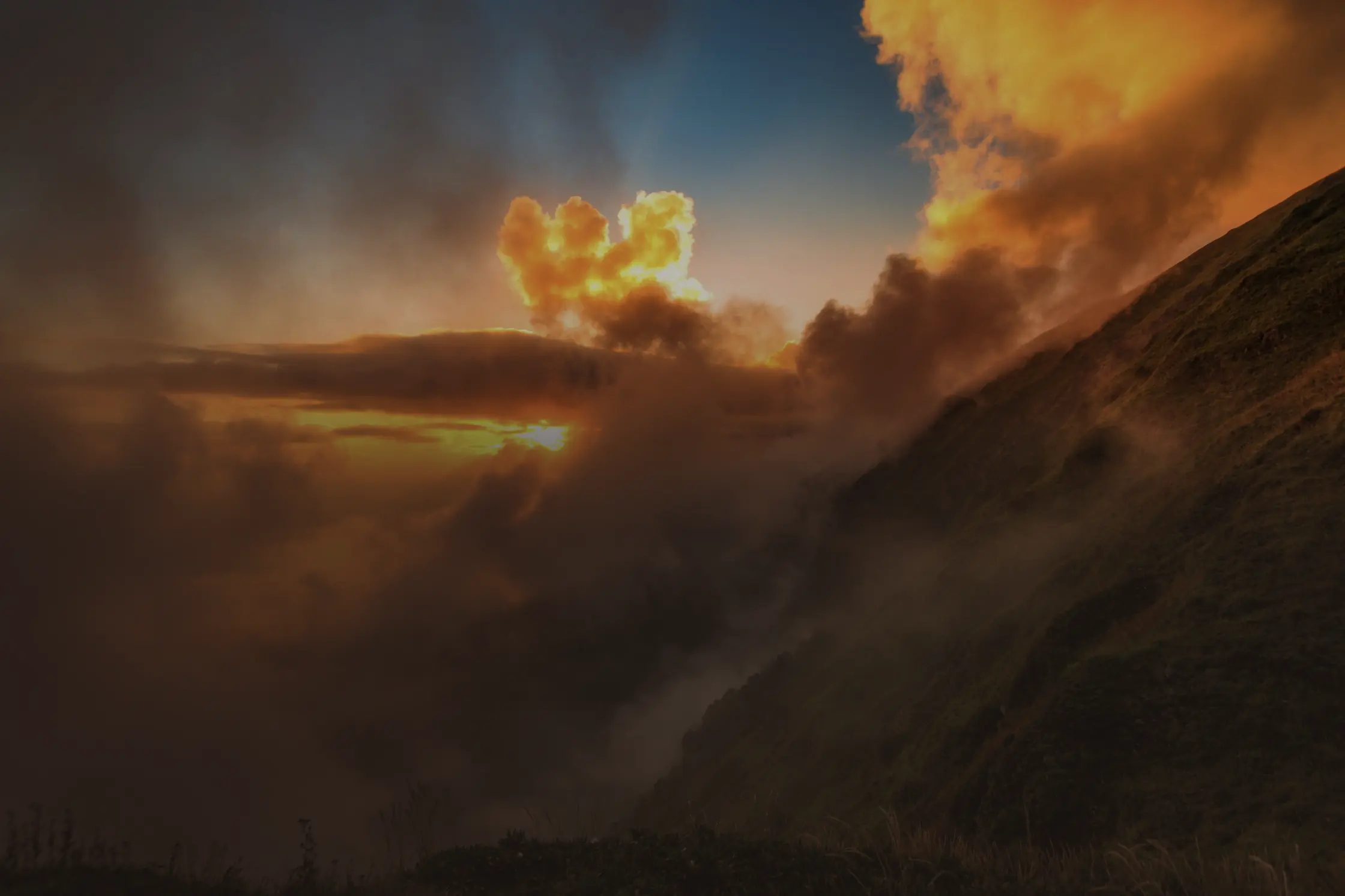 Un versant d’herbe rase au-dessus d’une mer de nuages, le soleil couchant qui allume les crêtes.