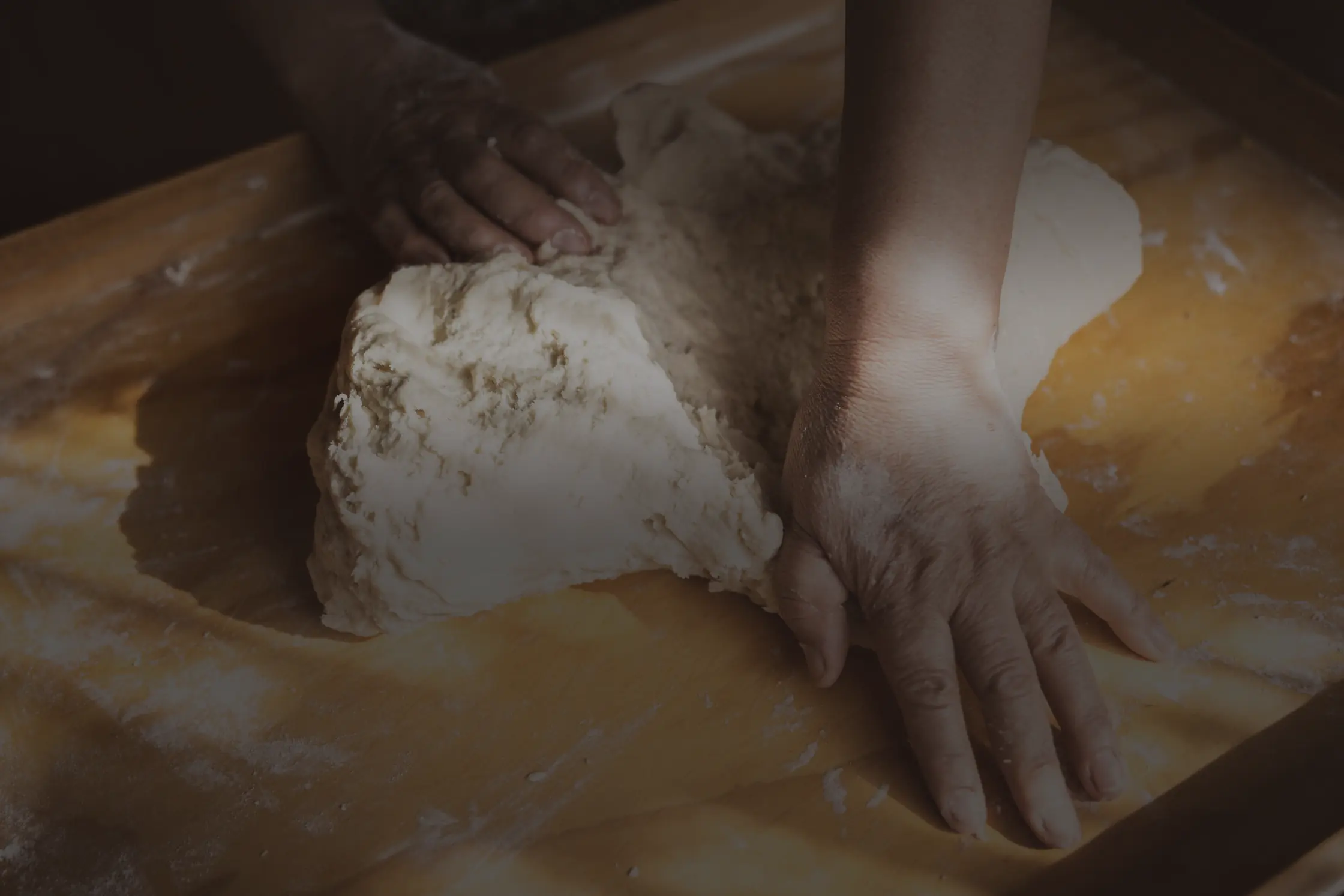 Deux mains qui pétrissent une pâte à pain sur une planche de bois farinée.