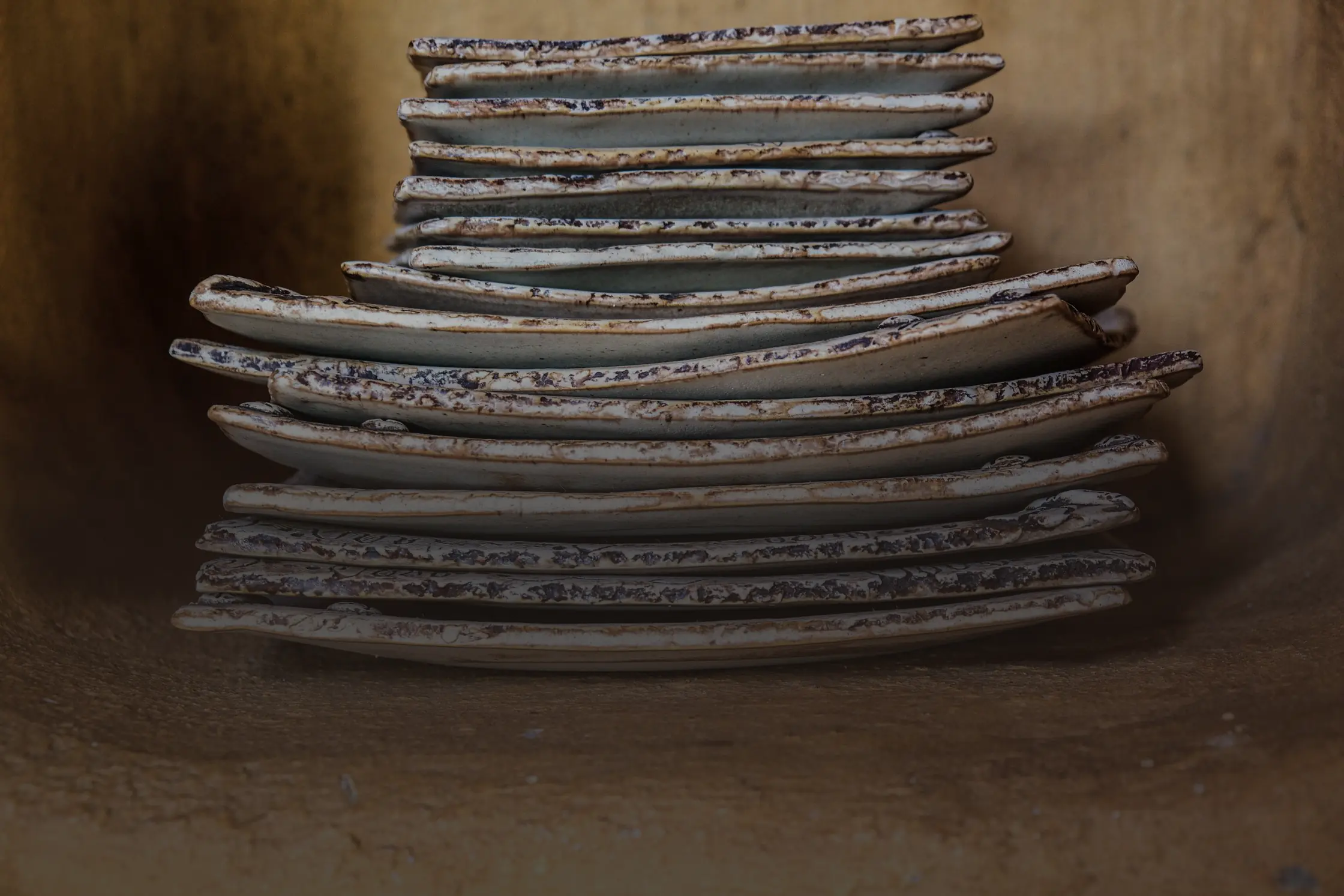 Une pile d’assiettes de grès tournées à la main, aux bords irréguliers, rangées dans une niche de bois.